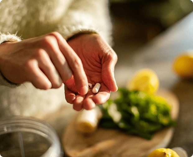 Hands holding pills near fresh vegetables.